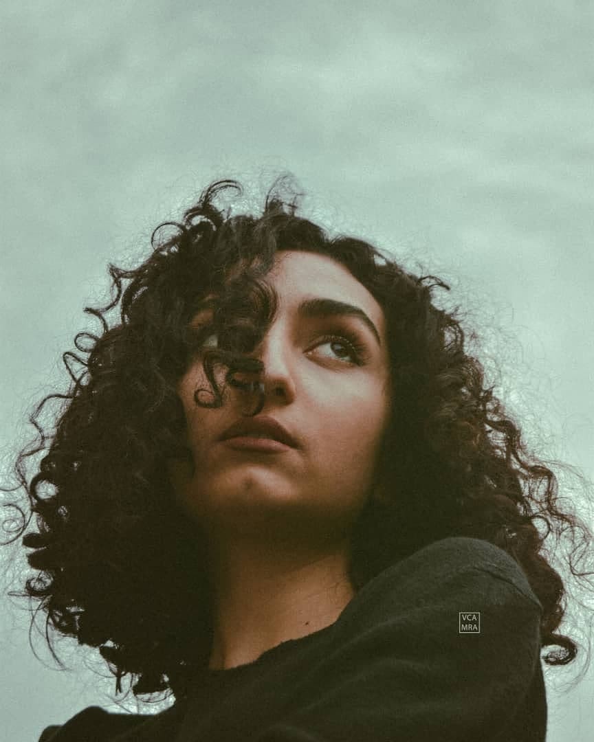 Woman with curly dark hair looking up against an overcast sky