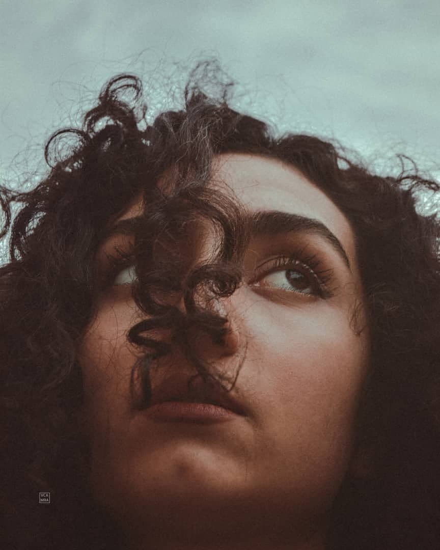 Close-up of a woman's face looking upward, dark curls falling across her nose