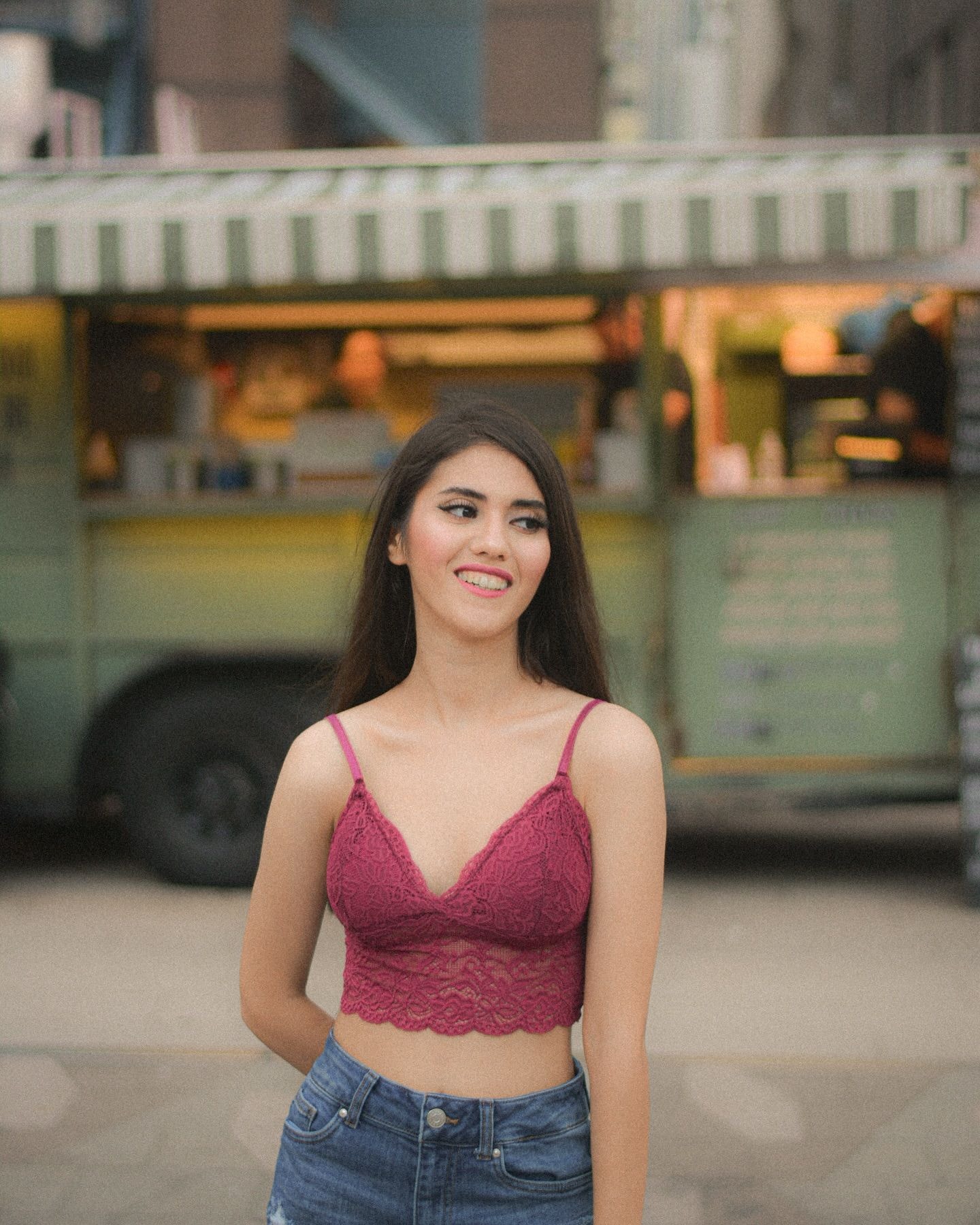 Smiling woman in a pink lace top standing in front of a green food truck with a striped awning