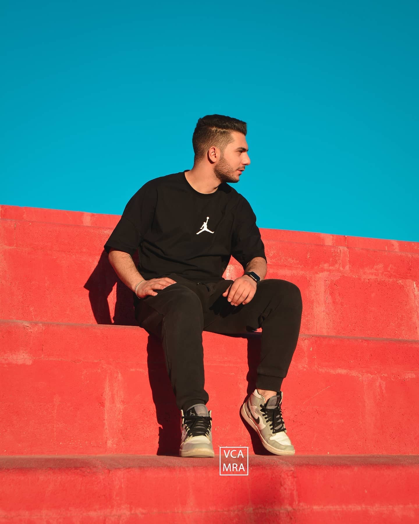 Man in a black t-shirt sitting on bright red concrete steps under a clear blue sky